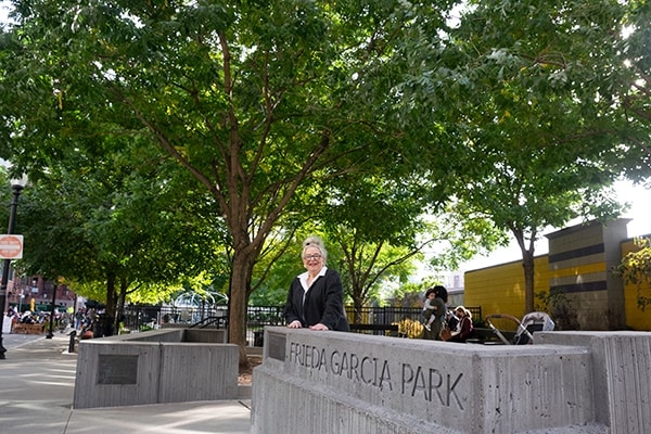 Frieda Garcia in front of park with her name engraved in cement, families at playground in background.